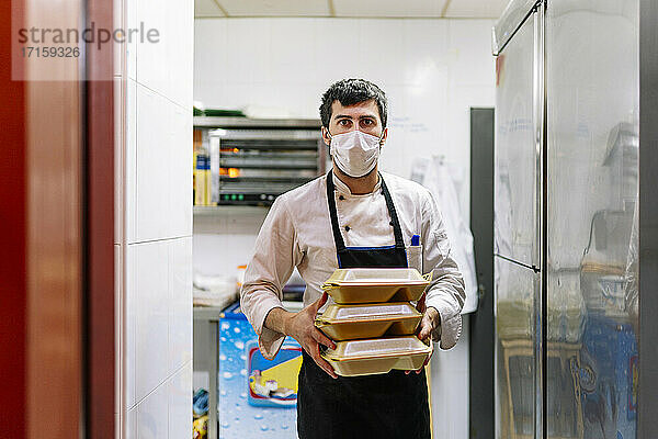 Junger Koch in Schürze mit Lebensmittelbehältern bei der Arbeit in einem Restaurant während einer Pandemie