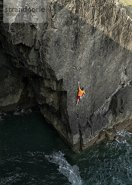Männlicher Felskletterer klettert an einer Klippe über Wasser