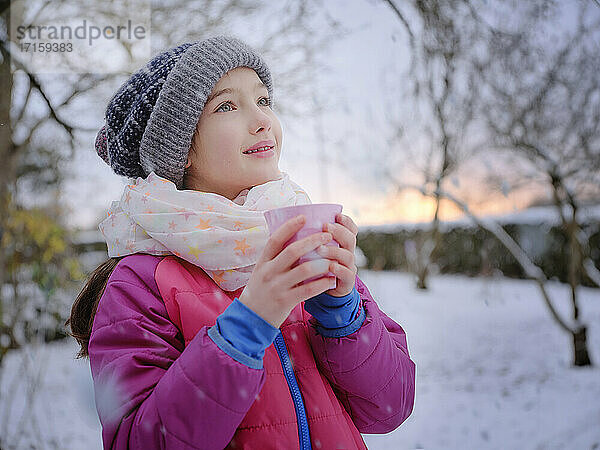 Thoughtful girl holding tea cup wearing warm clothing during sunset in winter
