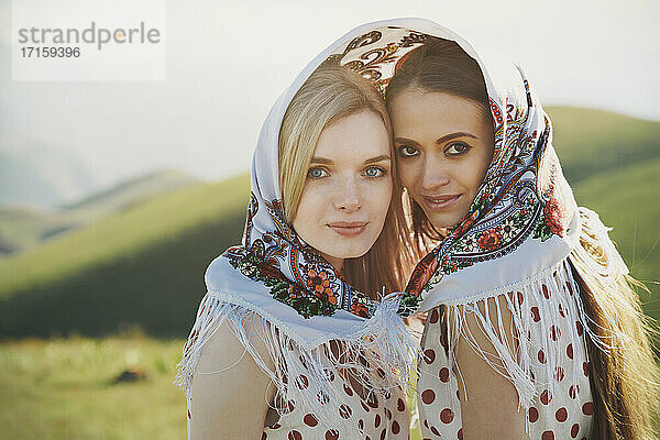 Beautiful lesbian couple with polka dot dress sharing headscarf during sunny day