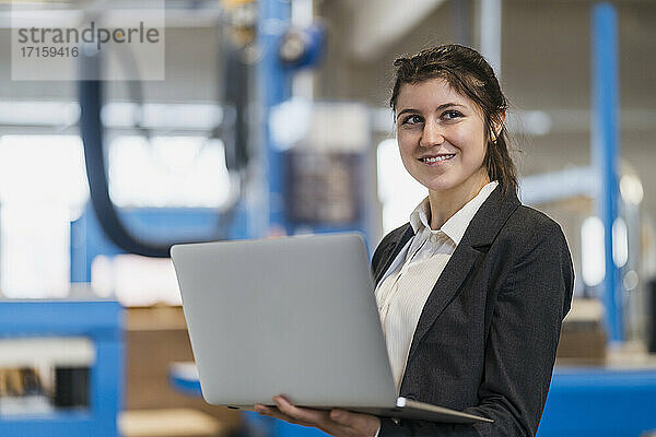 Young businesswoman smiling while using laptop standing at industry