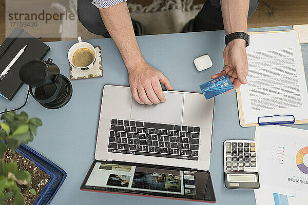 Geschäftsmann mit Kreditkarte beim Einkaufen über Laptop  während er zu Hause sitzt