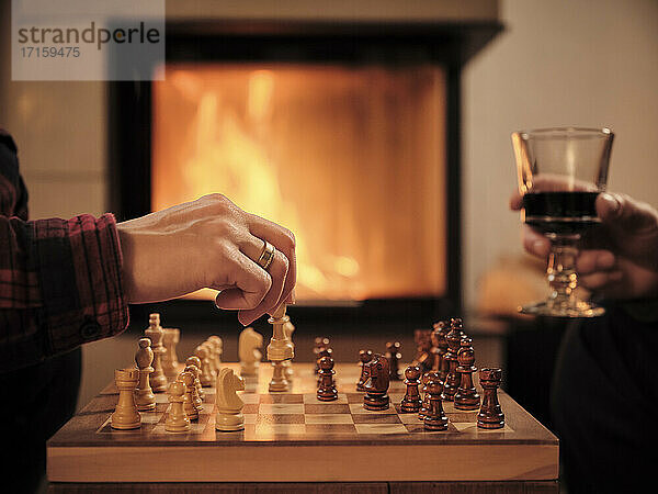 Reifer Mann mit Weinglas  während Frau am Kamin im Wohnzimmer Schach spielt