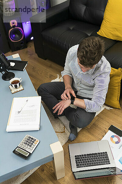 Geschäftsmann  der zu Hause sitzend seine Smartwatch überprüft