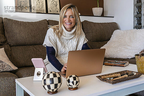 Glückliche Beraterin sitzt mit Laptop auf dem Sofa am Arbeitsplatz