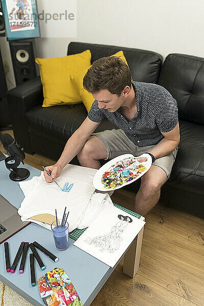 Männlicher Künstler  der zu Hause sitzend auf Papier malt