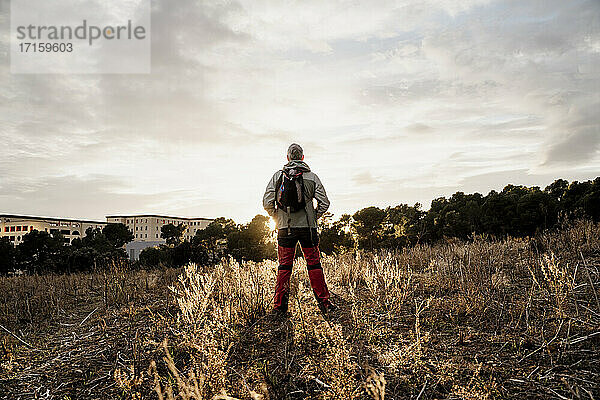 Älterer männlicher Wanderer steht auf einem landwirtschaftlichen Feld in der Landschaft bei Sonnenuntergang