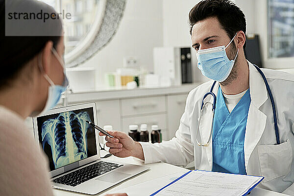 Male doctor explaining medical X-ray on laptop to female patient in clinic
