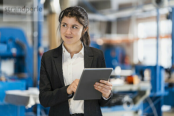 Smiling businesswoman with digital tablet looking away while standing at industry