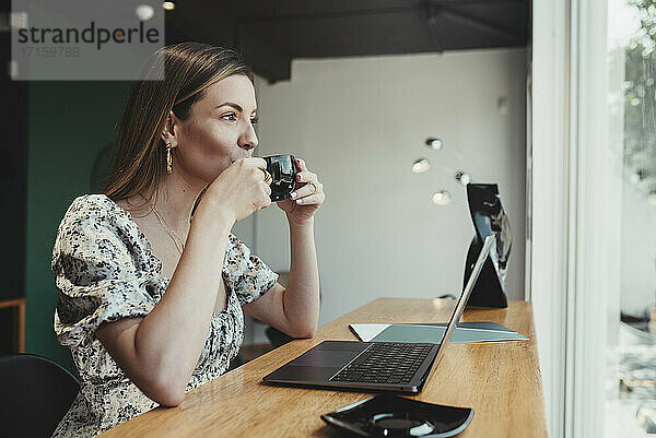 Geschäftsfrau mit Laptop auf dem Tisch  die Kaffee trinkt  während sie in einem Café sitzt