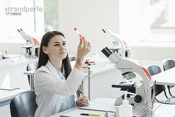 Junge Forscherin im weißen Kittel bei der Untersuchung einer Laborprobe