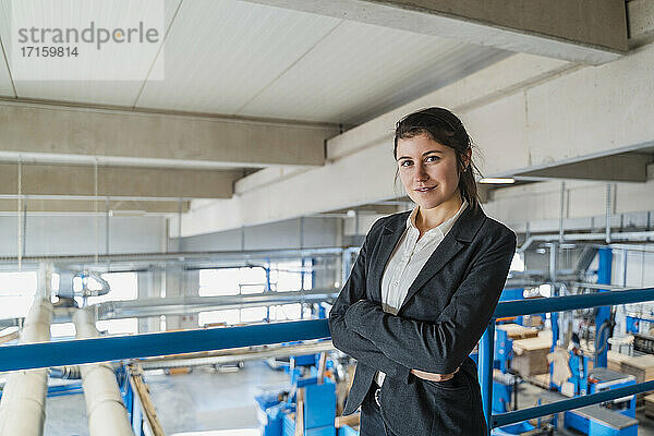 Smiling businesswoman with arms crossed standing by railing at industry