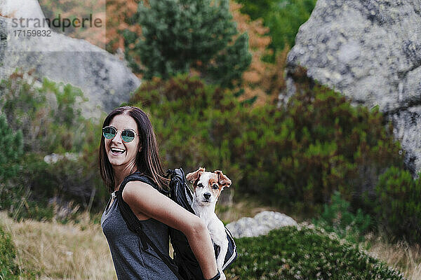 Fröhliche Frau mit Hund im Rucksack beim Wandern auf einem Berg