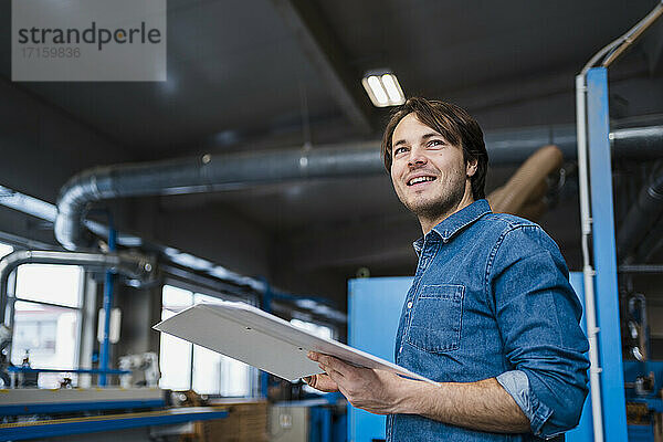 Male inspector with file smiling while standing at industry