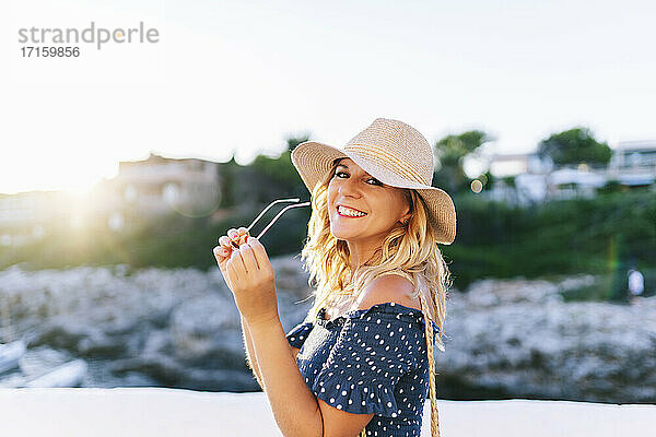 Lächelnde  schöne Frau mit Sonnenbrille vor einem klaren Himmel im Dorf Binibeca  Menorca  Spanien