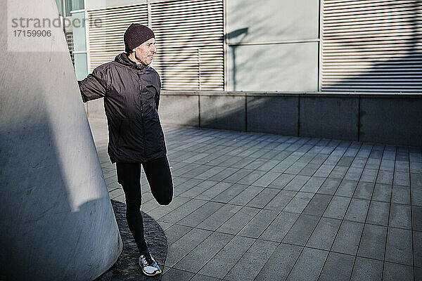 Male runner doing stretching exercise by wall during sunny day