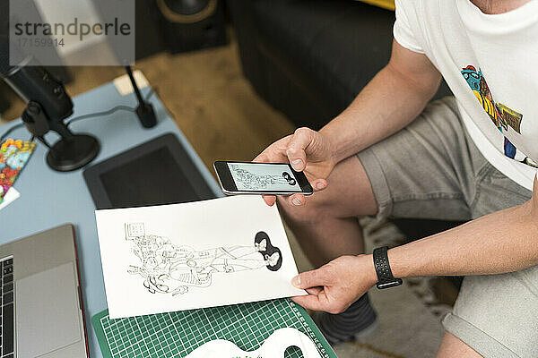 Künstler  der zu Hause sitzend mit seinem Handy ein Designfoto aufnimmt