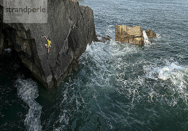 Junger männlicher Felskletterer klettert auf Felsen gegen das Meer