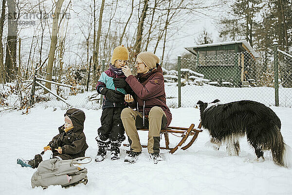 Mutter  die ihre Tochter füttert  während sie im Winter im Schnee ein Wochenende mit der Familie verbringt