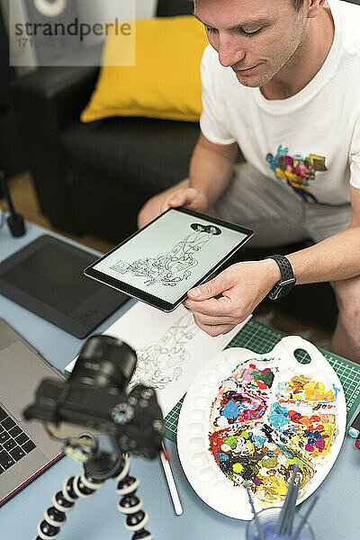 Künstler schaut auf ein digitales Tablet  während er zu Hause über einen Laptop live streamt
