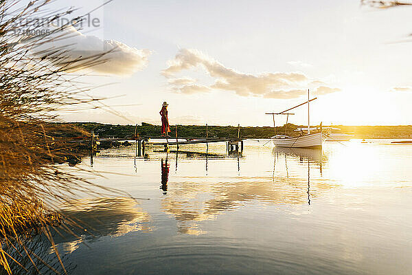 Frau  die bei Sonnenuntergang auf dem Pier steht und die Aussicht betrachtet