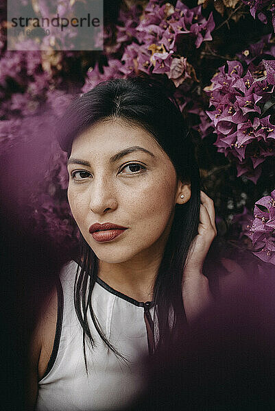 Schöne Frau mit Hand im Haar gegen rosa Blumen im Park