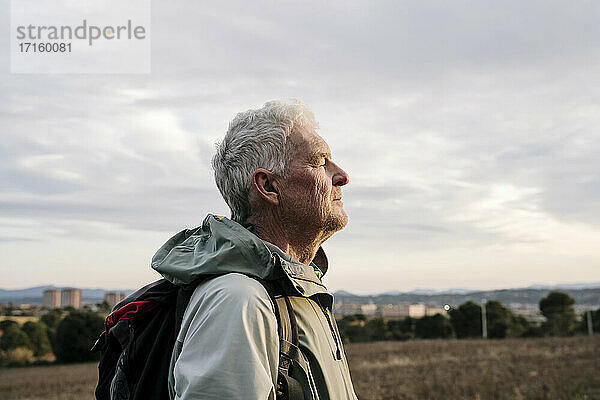 Älterer männlicher Wanderer mit geschlossenen Augen in der Landschaft bei Sonnenuntergang