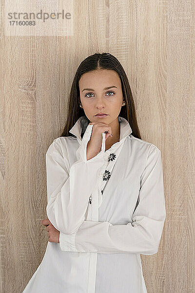 Stylish Teenager-Mädchen trägt weiße Jacke posiert gegen Holzwand zu Hause