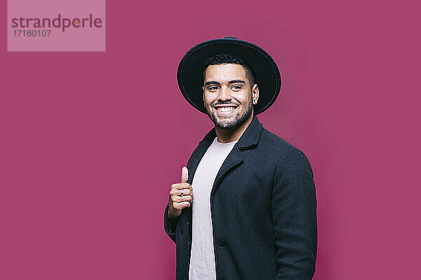 Smiling man in hat wearing blazer jacket while looking away against pink background
