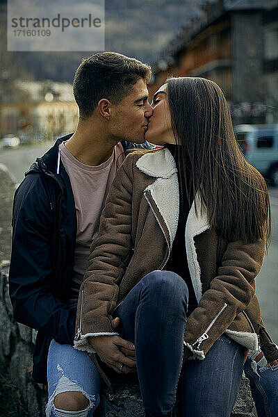 Junges Paar  das sich mit geschlossenen Augen küsst  während es in der Stadt sitzt