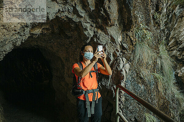 Hiker wearing face mask using mobile phone while standing by underpass at Cares Trail in Picos De Europe National Park  Asturias  Spain
