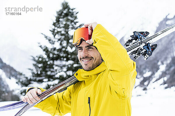 Smiling man with ski looking away while standing on snow covered valley