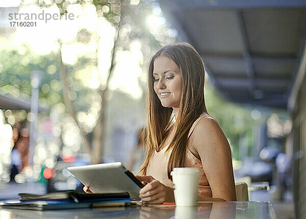 Female entrepreneur using digital tablet while sitting at sidewalk cafe