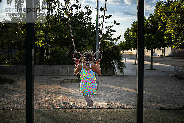 Girl hanging on gymnastic rings on playground at park