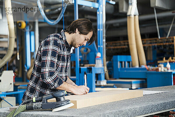 Industrial worker measuring plank while working at industry