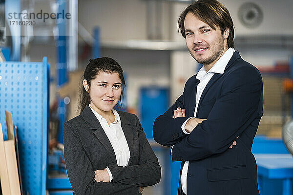 Confident business people smiling while standing with arms crossed at industry
