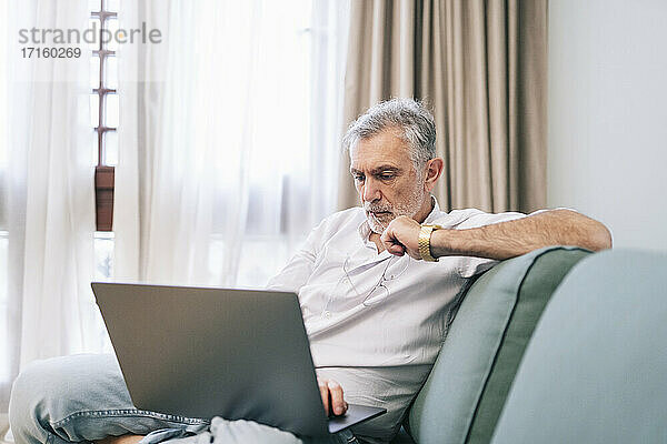 Concentrated man using laptop while sitting on sofa in hotel room
