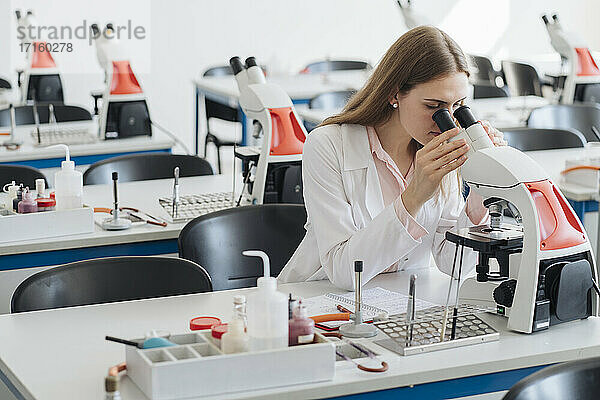 Junge Forscherin im weißen Kittel bei der Arbeit mit dem Mikroskop im Labor