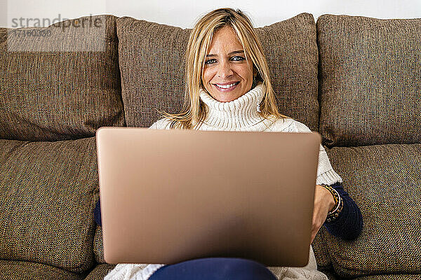 Lächelnde weibliche Therapeutin sitzt mit Laptop auf dem Sofa am Arbeitsplatz