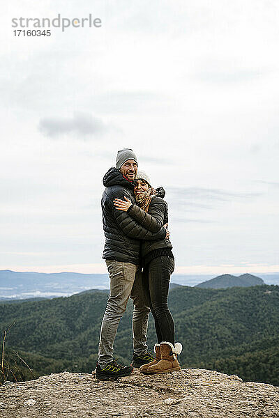 Glückliches Paar umarmt einander am Aussichtspunkt gegen den Himmel