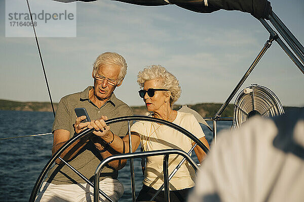 Senior Paar navigieren Richtung auf Smartphone beim Segeln in Boot während des sonnigen Tages