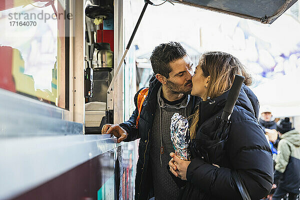 Heterosexuelles Paar  das sich beim Kauf einer verpackten Bestellung im Straßencafé küsst