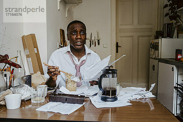 Nachdenklich männlichen Unternehmer mit Papier Dokument mit Nudeln am Tisch im Wohnzimmer