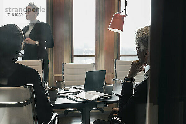 Männliche und weibliche Kollegen hören einer Geschäftsfrau zu  die während einer Besprechung im Vorstandszimmer die Strategie erklärt
