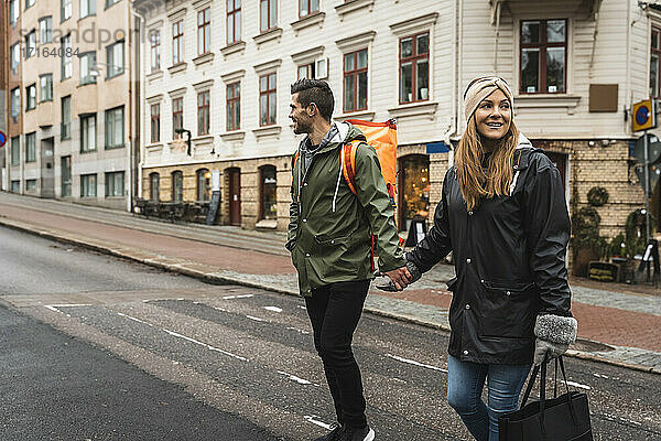 Lächelndes Paar hält Hände beim Überqueren der Straße in der Stadt