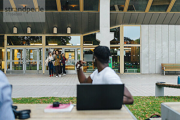 Männlicher Student mit Blick auf Freunde zu Fuß in College-Campus