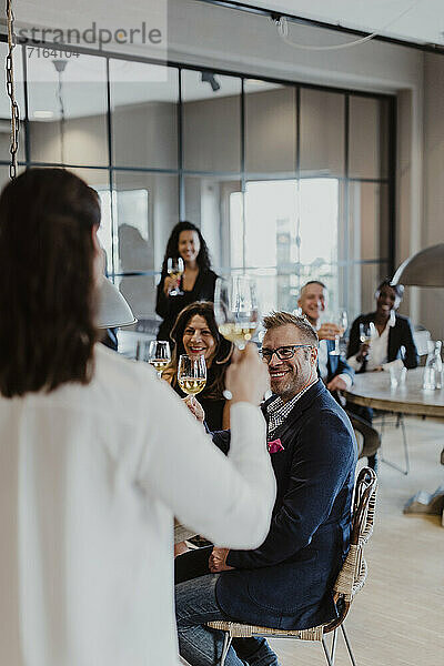 Weibliche Unternehmerin mit Weinglas blickt auf Kollegen während der Firmenfeier