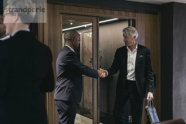 Senior Geschäftsmann schüttelt Hände mit männlichen Fachmann im Sitzungssaal während der Sitzung