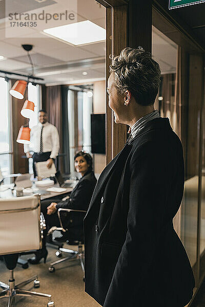 Seitenansicht einer reifen Geschäftsfrau  die durch eine Glaswand auf ihre Kollegen im Vorstandszimmer blickt