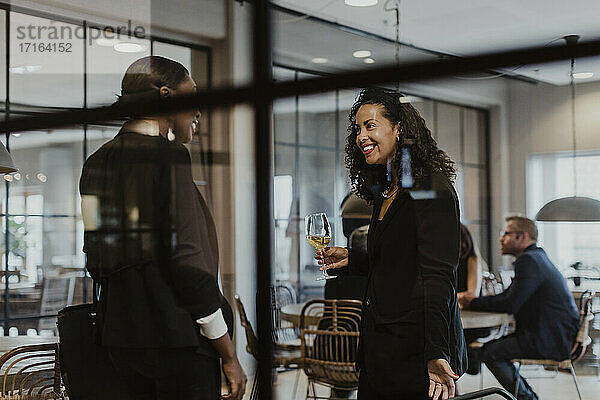 Lächelnde weibliche Kollegen  die sich unterhalten  während sie ein Weinglas im Büro während einer Party halten
